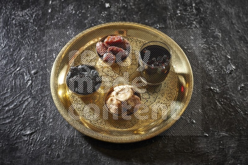 Dried fruits in metal bowls with tamarind on a tray in dark setup
