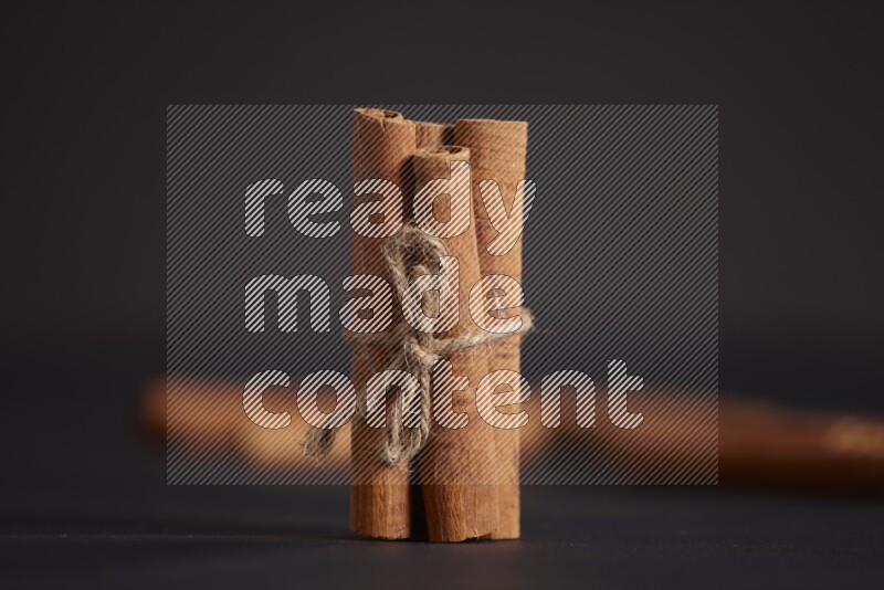 4 Cinnamon sticks stacked and bounded with more sticks in the background on black flooring