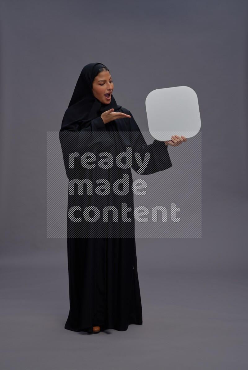 Saudi woman wearing Abaya standing holding social media sign on gray background