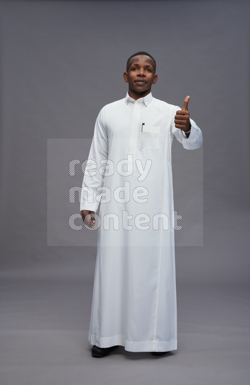 Saudi man wearing thob standing interacting with the camera on gray background