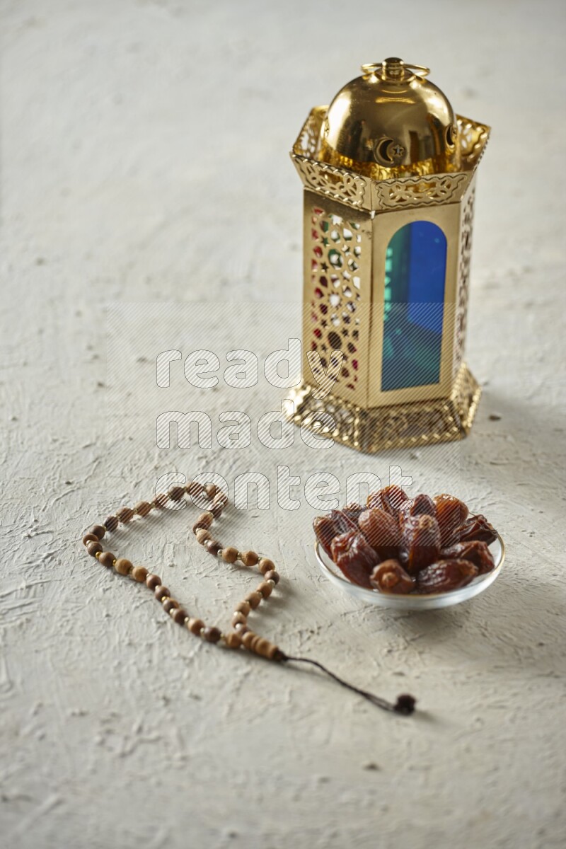 A golden lantern with different drinks, dates, nuts, prayer beads and quran on textured white background