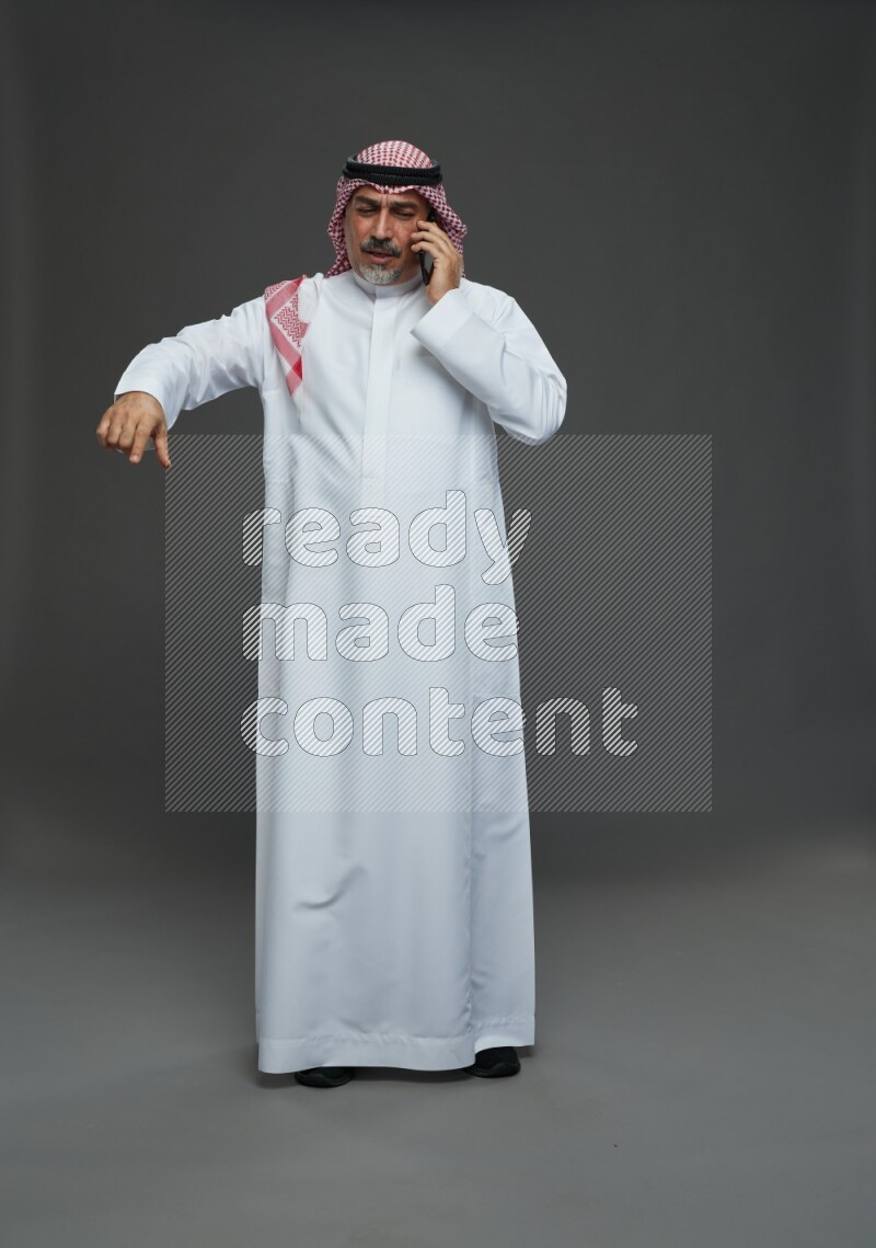 Saudi man with shomag Standing talking on phone on gray background