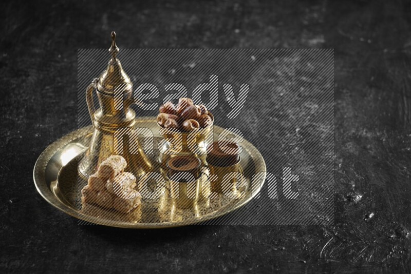 Oriental sweets with dates and a drink on a metal tray in a dark setup