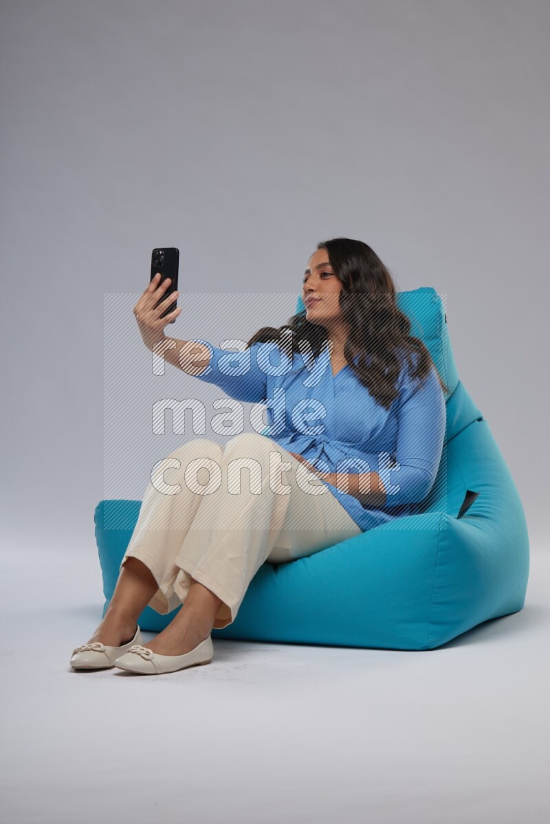 A woman sitting on a blue beanbag and taking selfie