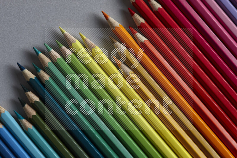 A collection of colored pencils arranged showcasing a gradient of different hues on grey background