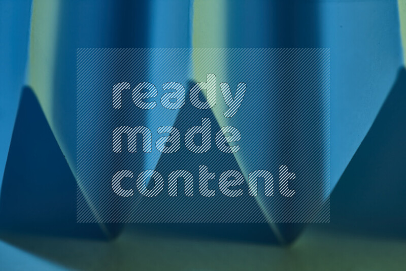 A close-up abstract image showing sharp geometric paper folds in green and blue gradients