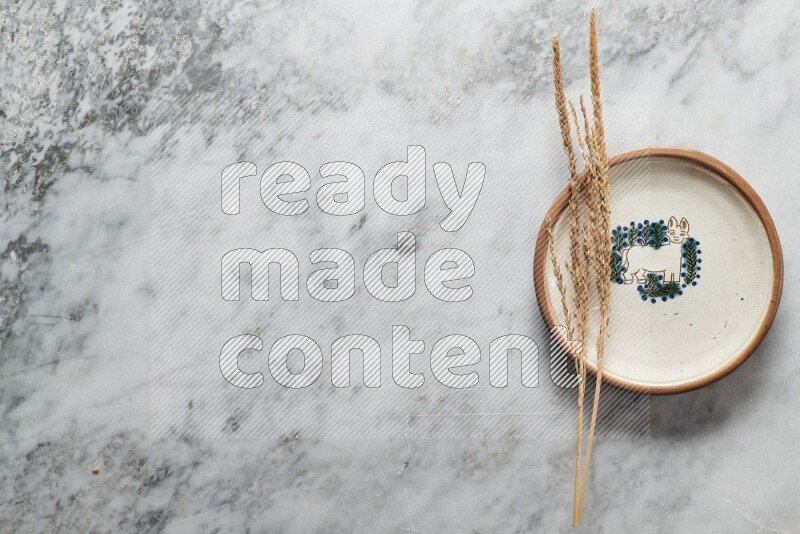Wheat stalks on decorative pottery plate on grey marble background