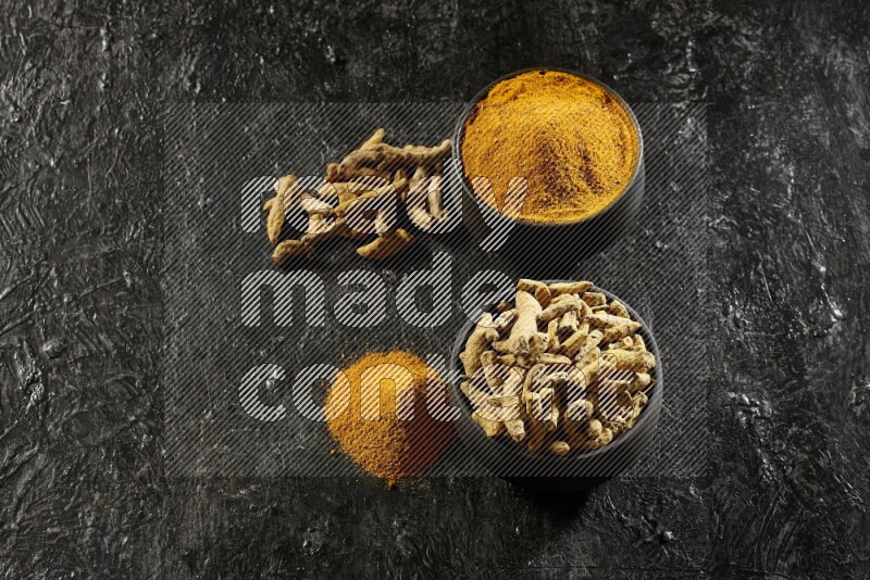 وعاءان من الفخار باللون الأسود، أحدهما ممتلئ ببودرة الكركم والآخر ممتلئ بأصابع كاملة من الكركم المجفف على خلفية سوداء