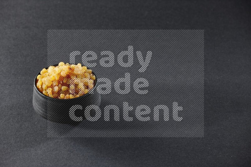A black pottery bowl full of raisins on a black background in different angles