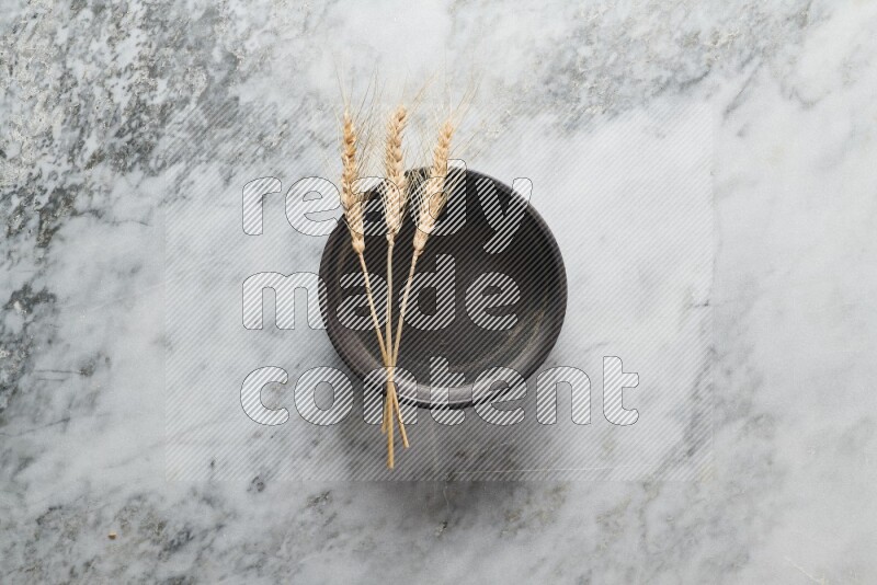 Wheat stalks on black pottery oven plate on grey marble background