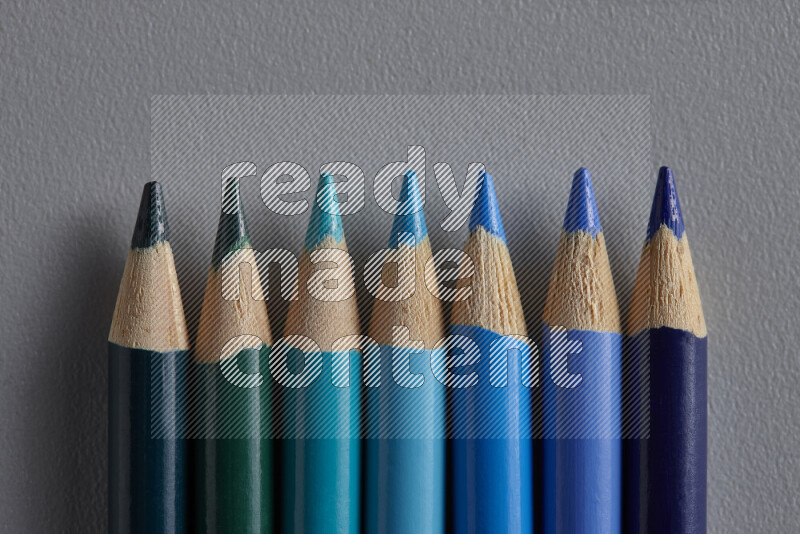 A collection of colored pencils arranged showcasing a gradient of blue hues on grey background