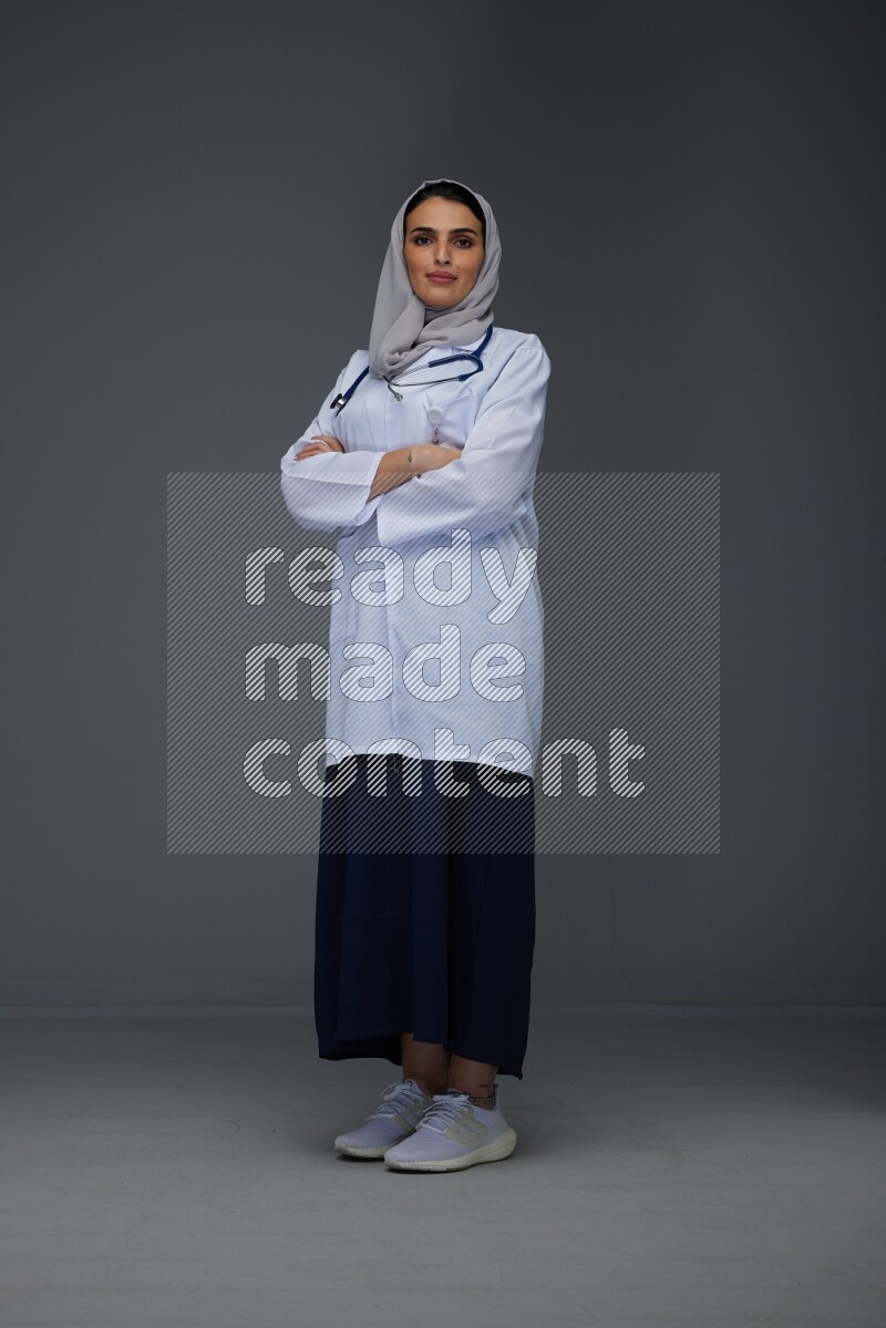 A female doctor wearing a light gray head scarf standing on grey background.