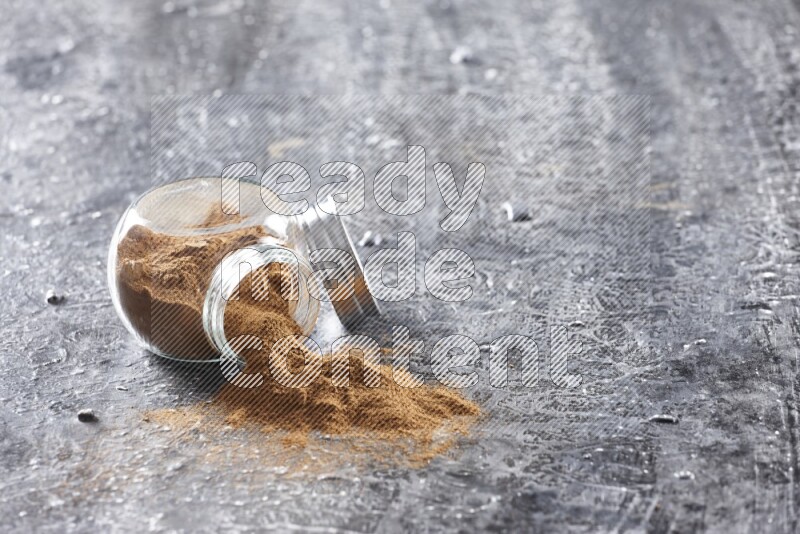 Flipped herbal glass jar full of cinnamon powder on textured black background