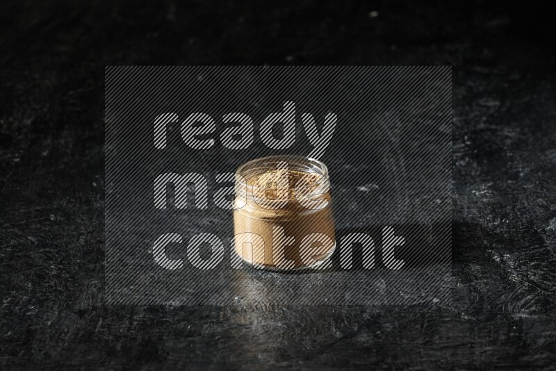 A glass jar full of allspice powder on a textured black flooring