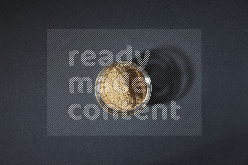 A glass bowl full of cumin powder on black flooring