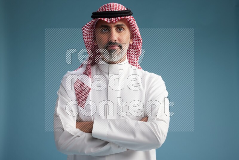 Saudi man wearing thob and shomagh posing to the camera on blue background