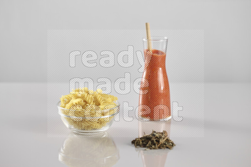 Raw pasta with tomatoe pasta with different ingredients such as cherry tomatoes, basil, garlic, bay laurel, cardamom, white pepper, black pepper, red chilis and wheat stalks on light grey background