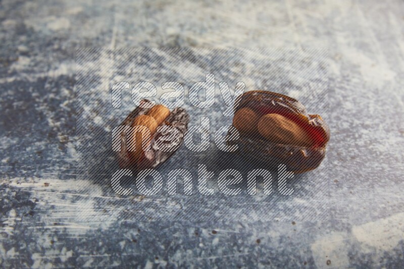 two almond stuffed madjoul dates on a rustic blue background