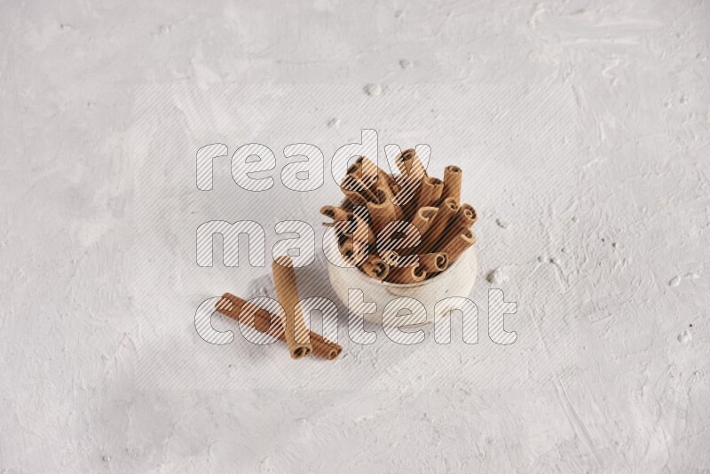Cinnamon sticks in a beige bowl and more sticks beside it on white background