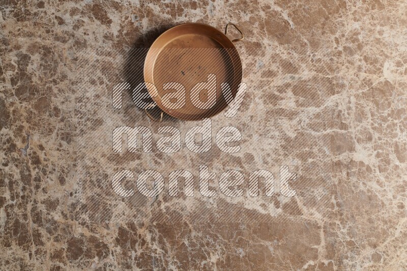 A small copper pan on beige marble background