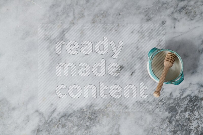 وعاء فخاري متعدد الألوان مع ملعقة عسل خشبية بداخله على خلفية من الرخام الرمادي