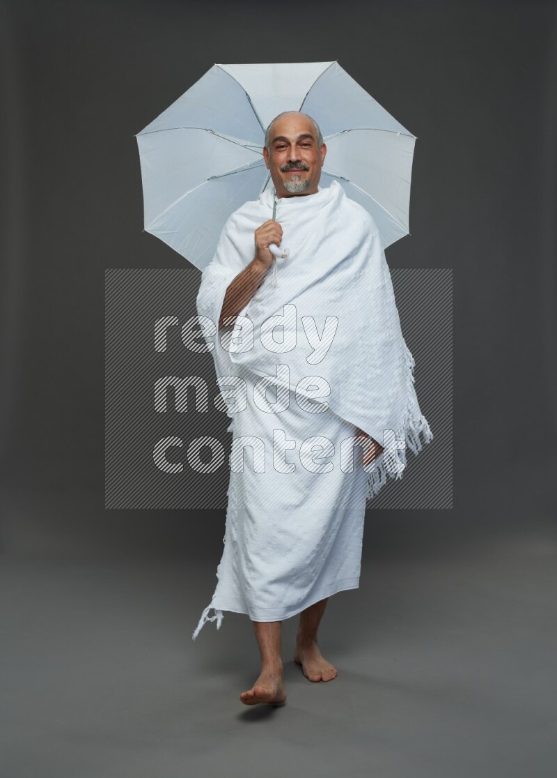 A man wearing Ehram Standing holding umbrella on gray background