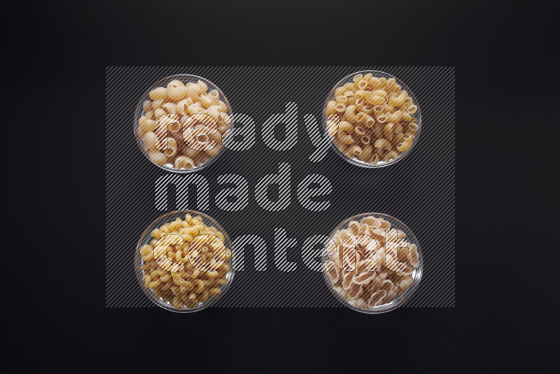 Different pasta types in glass bowls on black background