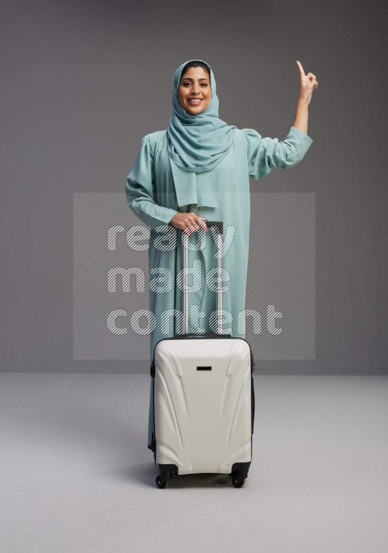 Saudi Woman wearing Abaya standing holding Travel bag on Gray background