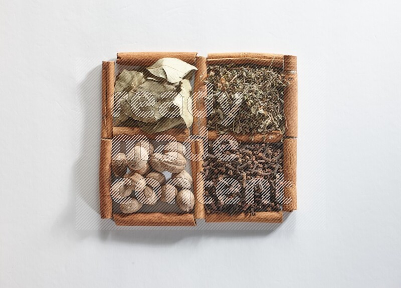 4 مربعات من أعواد القرفة ممتلئة بأوراق الغار والريحان المجفف والقرنفل وجوزة الطيب على أرضية بيضاء