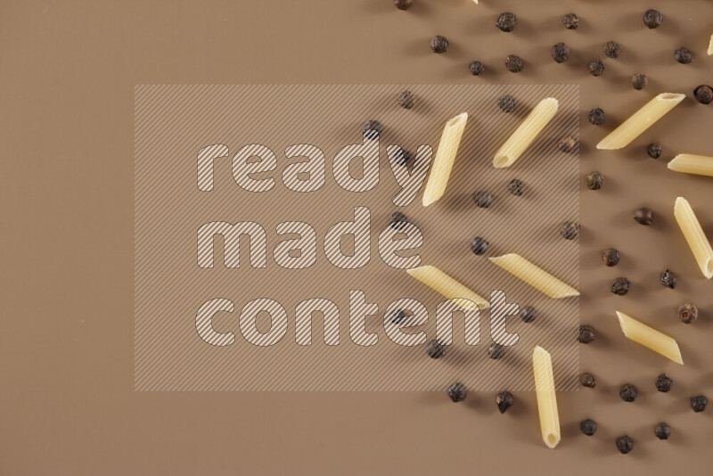 Raw pasta with different ingredients such as cherry tomatoes, garlic, onions, red chilis, black pepper, white pepper, bay laurel leaves, rosemary and cardamom on beige background