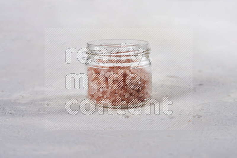 A glass jar full of coarse himalayan salt crystals on white background