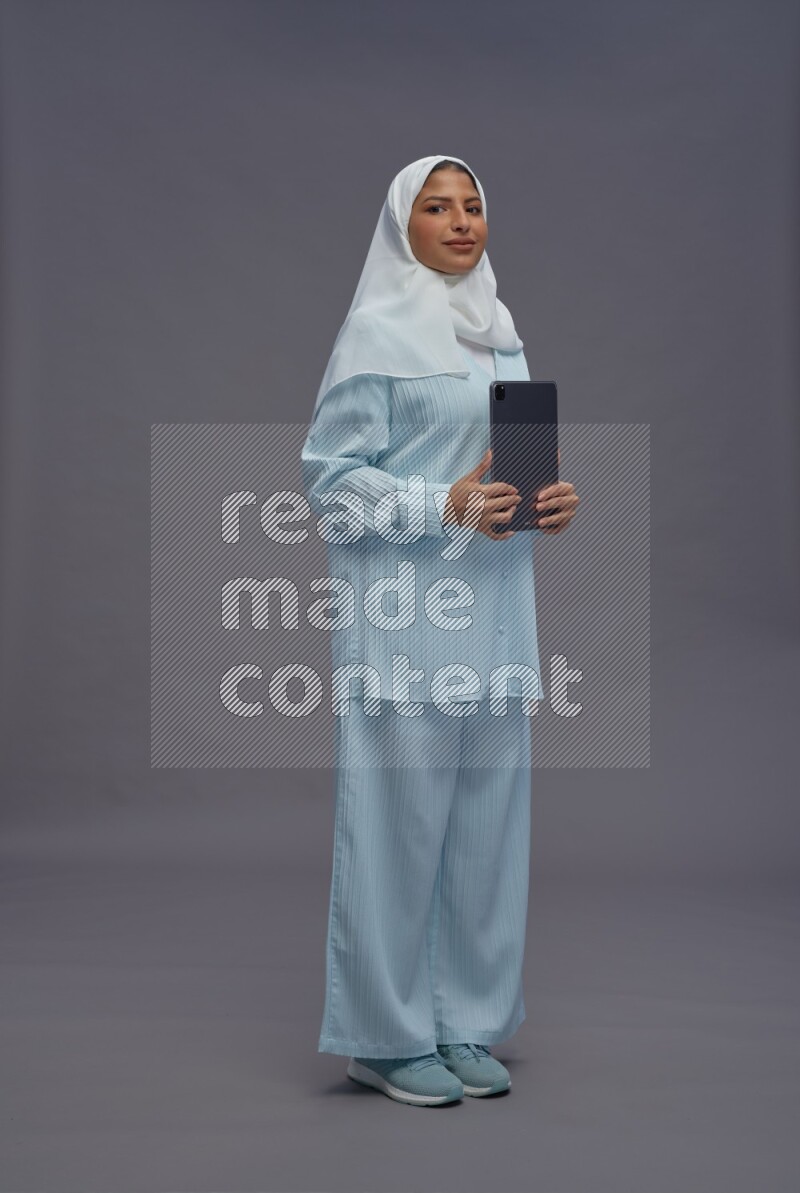 Saudi woman wearing hijab clothes standing working on tablet on gray background