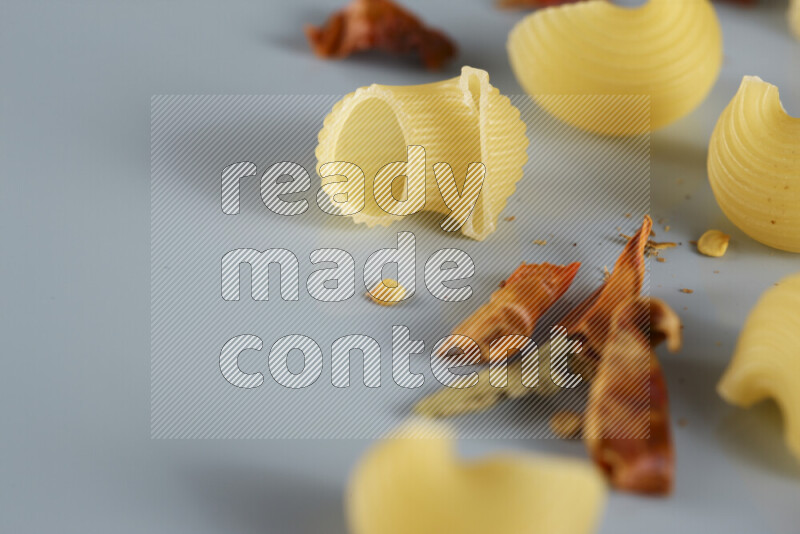 Raw pasta with different ingredients such as cherry tomatoes, garlic, onions, red chilis, black pepper, white pepper, bay laurel leaves, rosemary, cardamom and mushrooms on light blue background