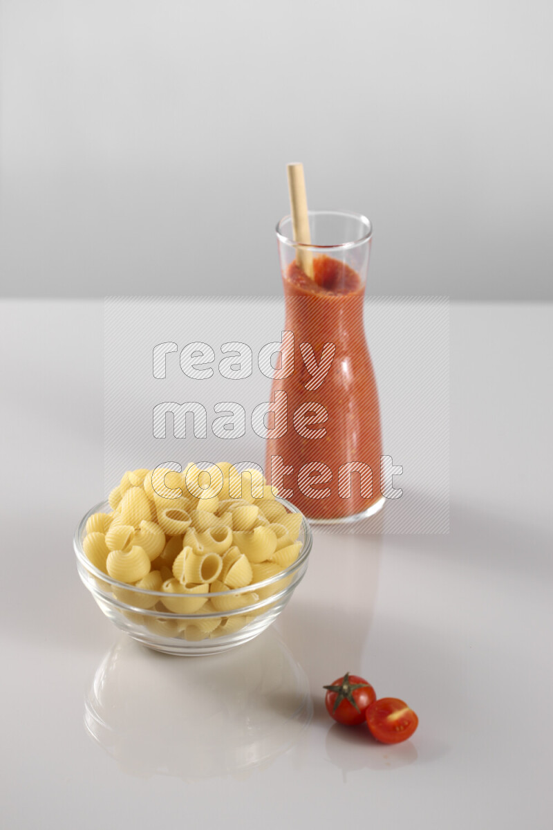 Raw pasta with tomatoe pasta with different ingredients such as cherry tomatoes, basil, garlic, bay laurel, cardamom, white pepper, black pepper, red chilis and wheat stalks on light grey background