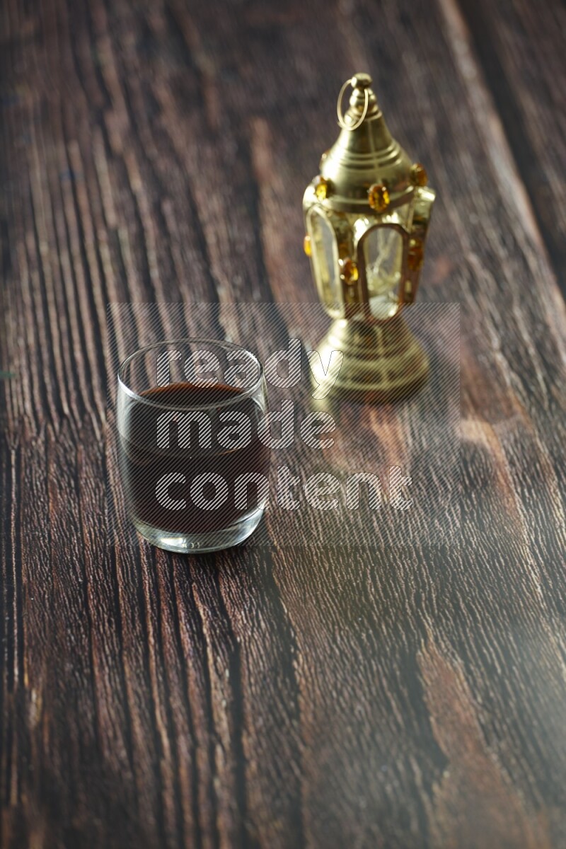 A golden lantern with different drinks, dates, nuts, prayer beads and quran on brown wooden background