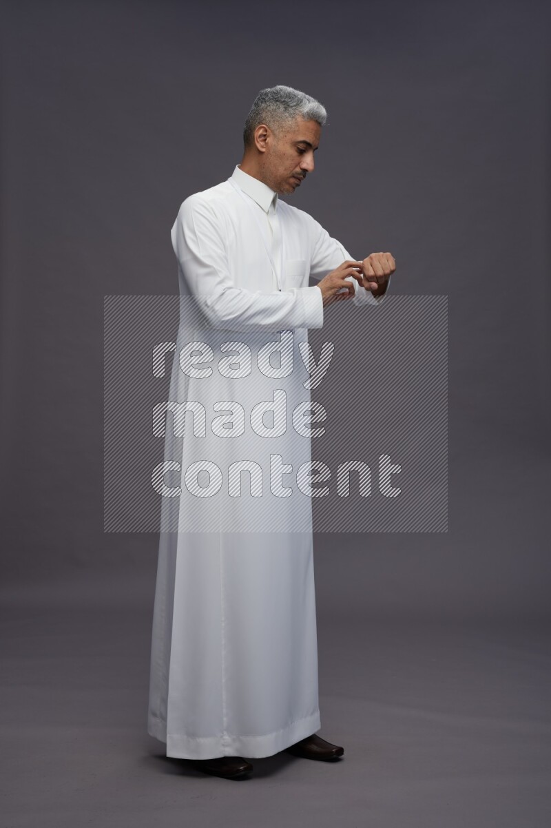Saudi man wearing thob with neck strap employee badge standing interacting with the camera on gray background