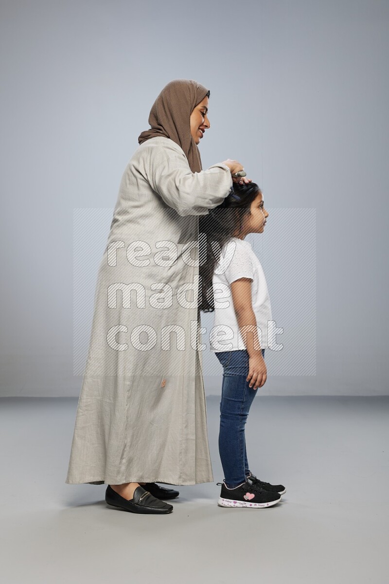 Mom standing styling hair for her daughter on gray background