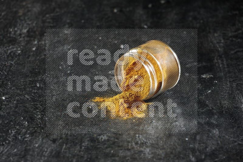 وعاء زجاجي مقلوب ممتلئ ببودرة الكركم والبودرة تناثرت منه على خلفية سوداء