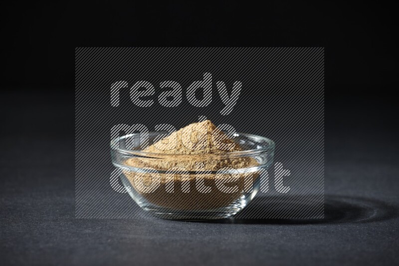 A glass bowl full of cumin powder on black flooring
