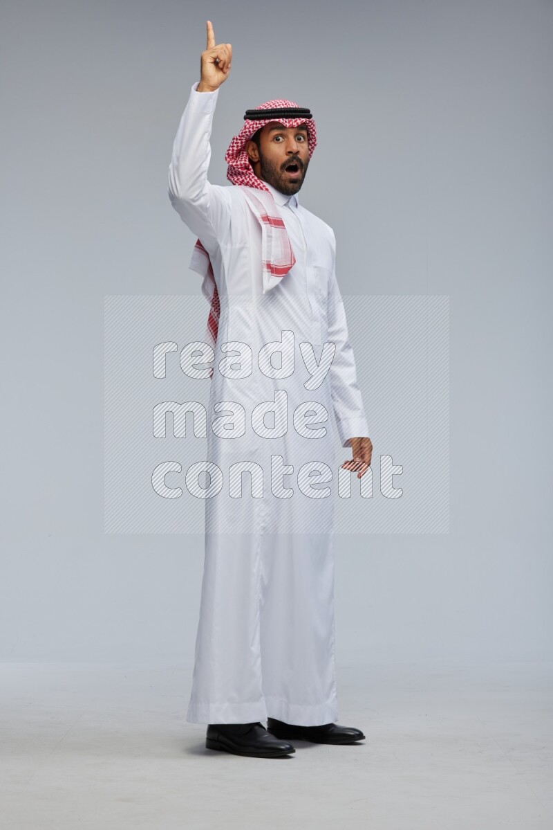 Saudi man Wearing Thob and shomag standing interacting with the camera on Gray background