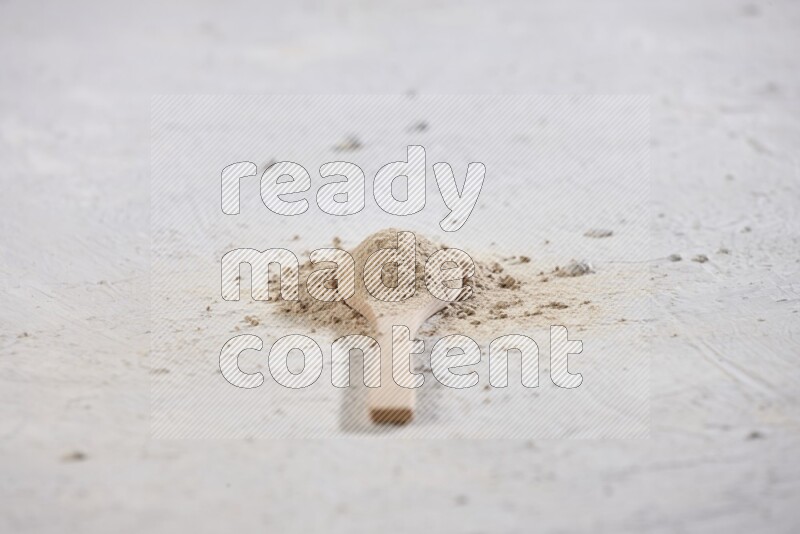 A wooden spoon full of garlic powder with scattered powder around it on a textured white flooring