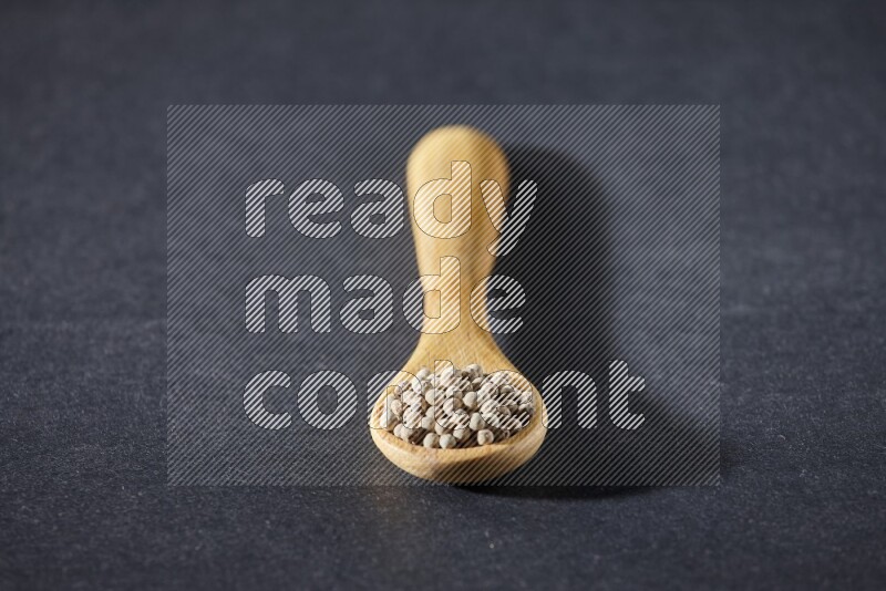 A wooden spoon full of white pepper beads on black flooring