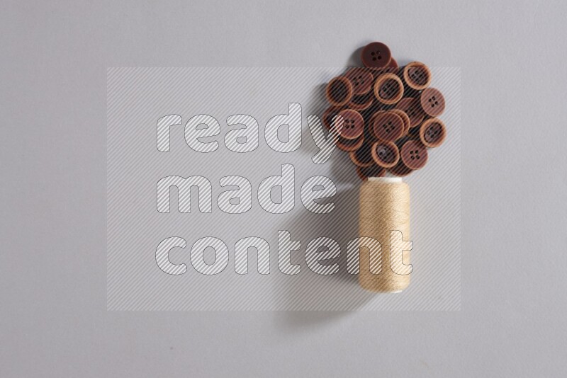 A beige sewing thread spool with colored buttons on grey background