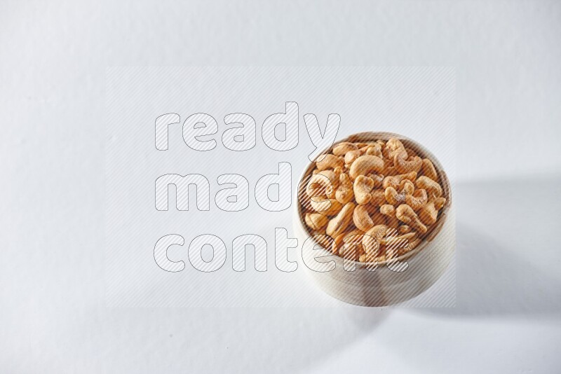 A beige ceramic bowl full of cashews on a white background in different angles