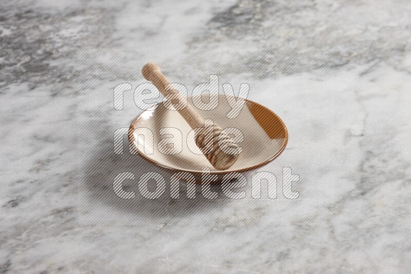 Multicolored pottery plate with wooden honey dipper in it on grey marble background