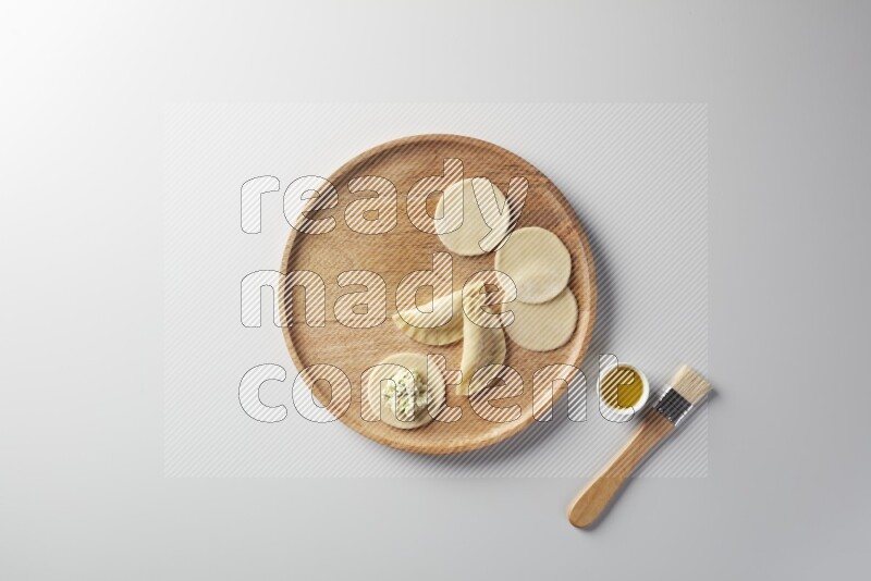 two closed sambosas and one open sambosa filled with cheese while oil with oil brush aside in a wooden dish on a white background
