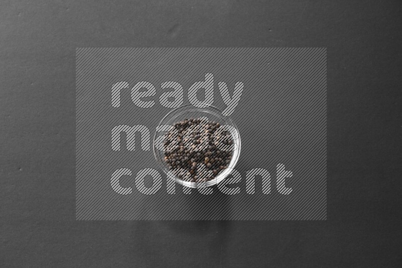 A glass bowl full of black peppers on black flooring