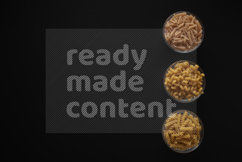 Different pasta types in 3 glass bowls on black background