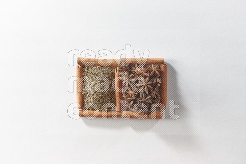 مربعان من أعواد القرفة ممتلئان باليانسون النجمي والكمون علي خلفية بيضاء