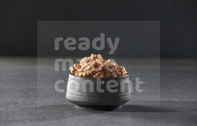 A black pottery bowl full of peeled walnuts on a black background in different angles